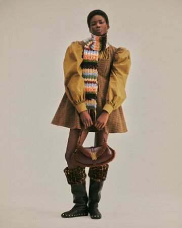 Model wearing checked dress and striped knit scarf from the Fall/Winter 2026 collection